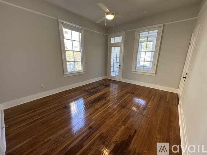 A room with wooden flooring and two windows.