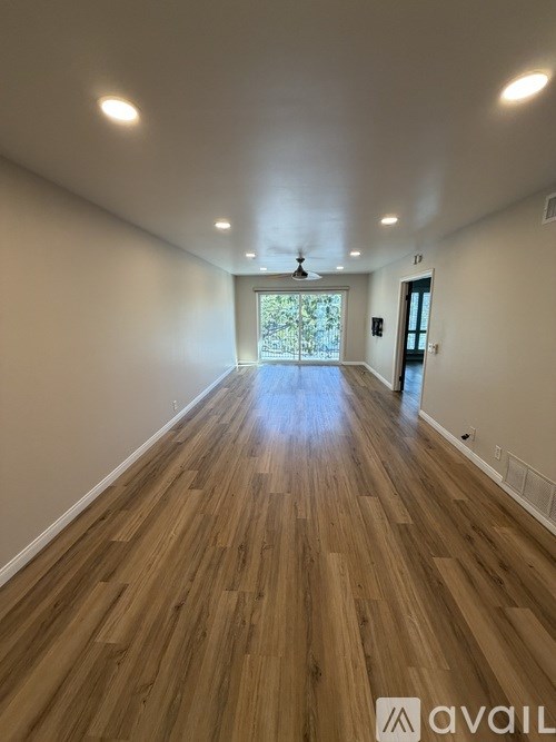 A long, empty room with wooden floors and a ceiling fan.