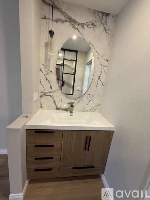 A bathroom with a marble wall and a round mirror above a sink.