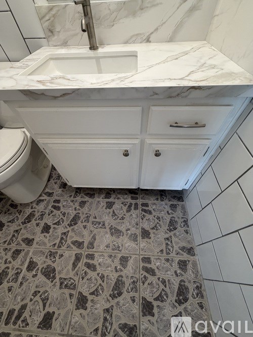 A white sink with a marble counter top and a toilet in a small bathroom.