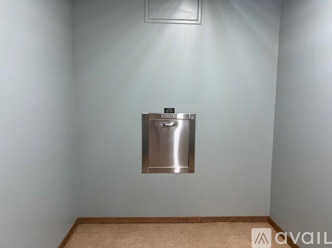 A stainless steel trash can is mounted on a wall in a room with a beige carpet.