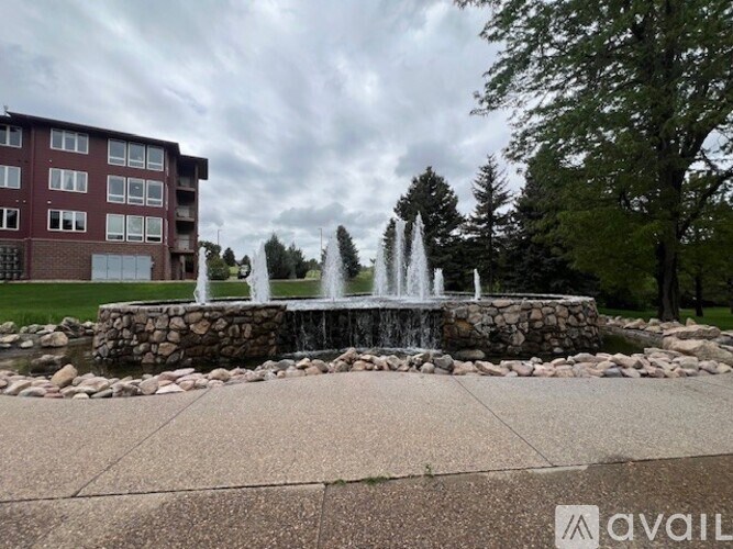 A fountain in the middle of a paved area with a building in the background.
