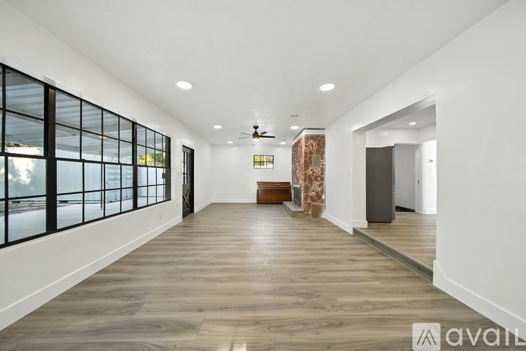 A spacious room with wooden flooring and large windows on one side.