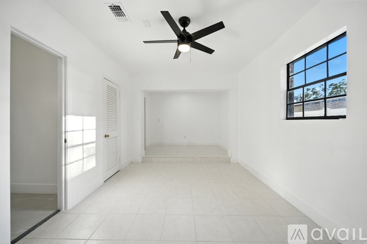 A spacious room with a ceiling fan and a window overlooking a building.