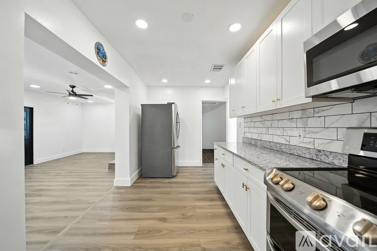 A modern kitchen with a stainless steel refrigerator and oven, white cabinets, and a marble backsplash.