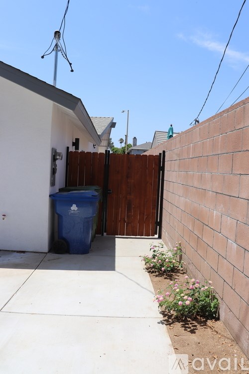 A blue trash bin sits on a concrete patio next to a wooden fence.