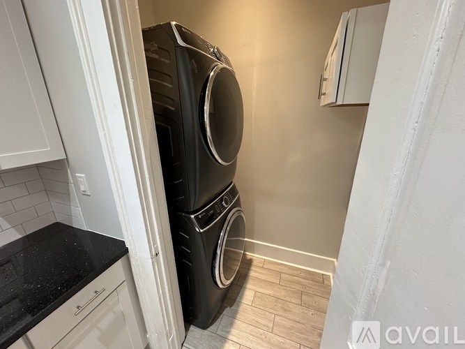 A black washing machine is stacked on top of a black dryer in a small laundry room.