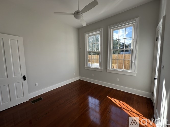 A room with a ceiling fan and two windows.
