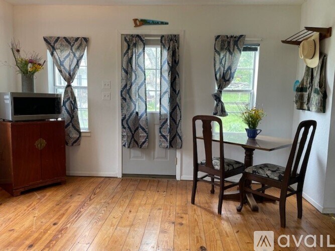 A room with a wooden floor, a television, a dining table with chairs, and a window with curtains.