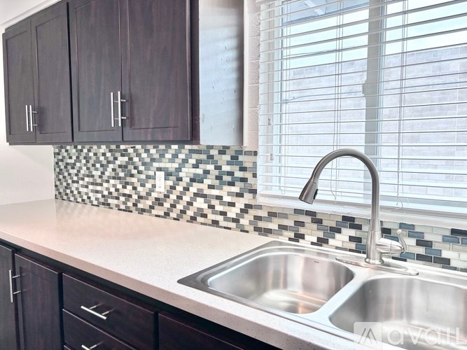 A kitchen with a checkered tile backsplash and a stainless steel sink.