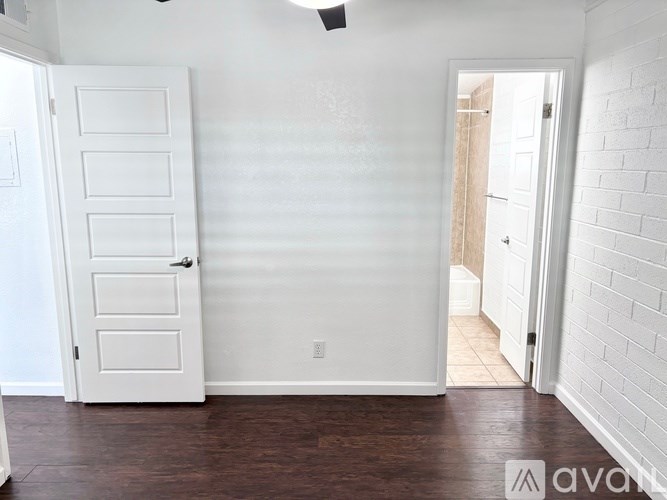 A white door with a white interior is on the left of a room with a wooden floor.