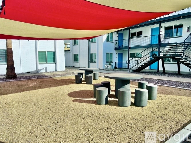 A large red and yellow umbrella is open over a sandy area with a table and chairs.