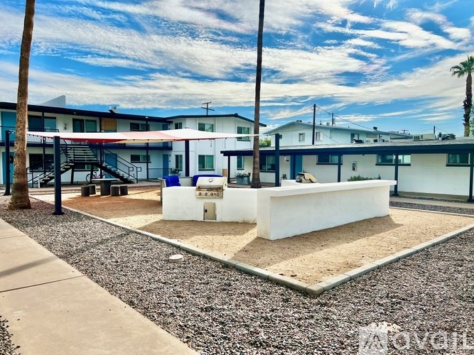 A playground area with a white sandbox in the middle of a gravel area with a building in the background.