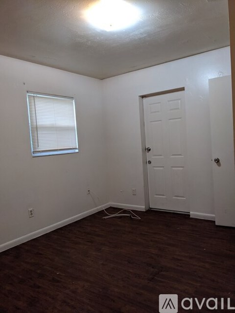 A room with a door, a window with blinds, and a wall socket.