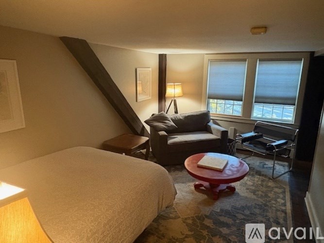 A bedroom with a bed, a chair, a couch, and a table with a book on it.