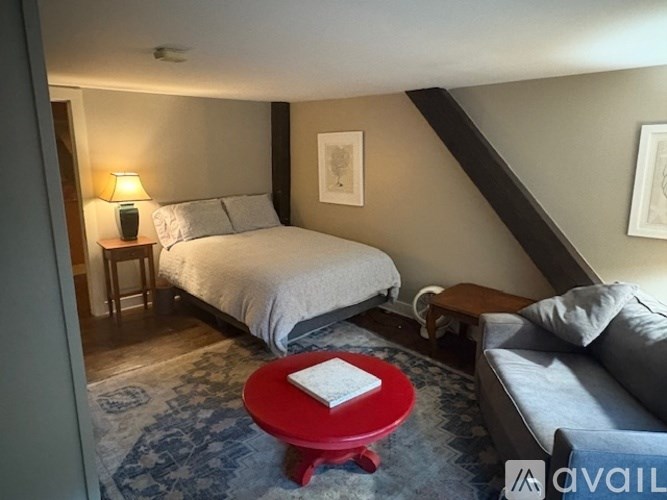 A bedroom with a bed, a couch, and a red table.