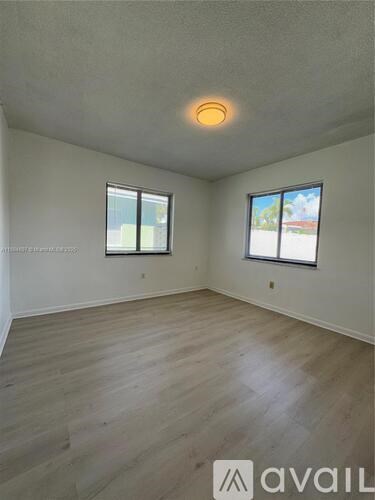 A room with wooden flooring and two windows.