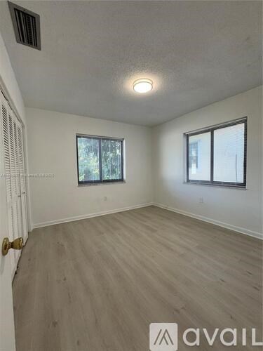 A room with wooden flooring and two windows.