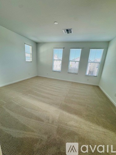 A room with beige carpet and three windows.