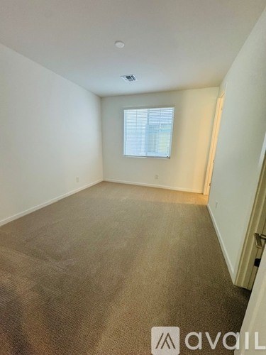 A carpeted room with a window and a door on the right side.
