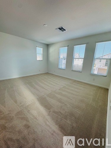 A room with beige carpet and three windows.