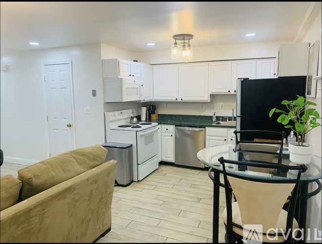 A kitchen with a black fridge, white cabinets, and a beige sofa.