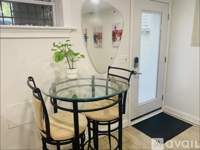 A glass table with two chairs and a potted plant sits in a room with a mirror and pictures on the wall.