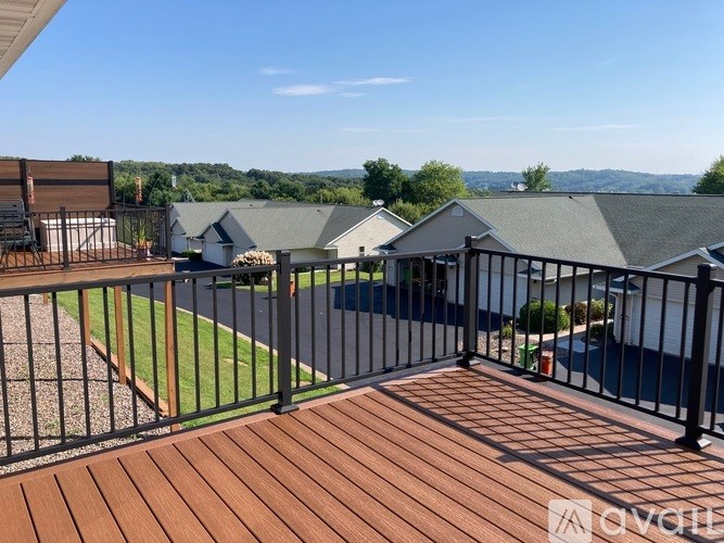A deck with a black railing and a wooden floor overlooks a grassy area and houses.