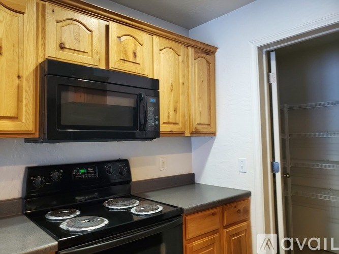 A black microwave oven is mounted above a black stove in a kitchen with wooden cabinets.