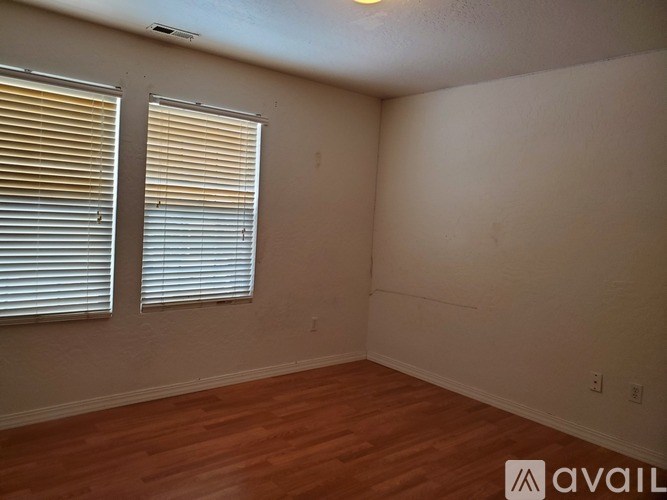 A room with wooden floors and two windows with blinds.