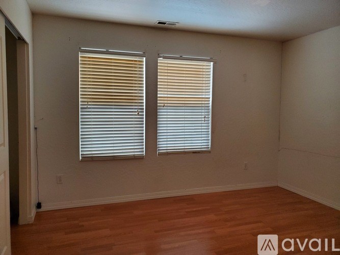 A room with wooden floors and two windows covered with blinds.