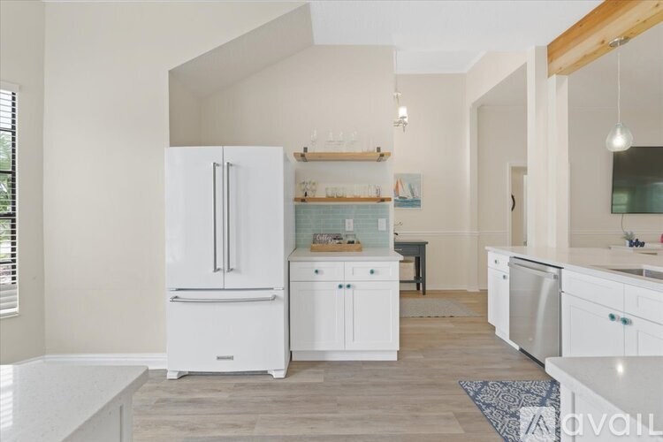 A white fridge in a kitchen with wooden floors and white cabinets.