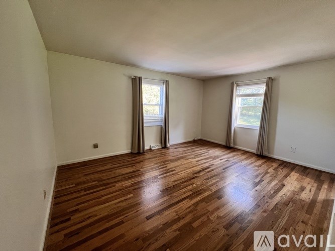 A room with wooden flooring and two windows with curtains.