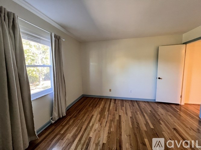 A room with wooden flooring and a window with curtains.
