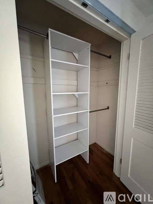 A tall white shelving unit with a black handle is in a room with white walls.