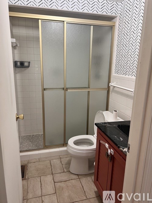 A bathroom with a toilet, a cabinet, and a shower with a glass door.