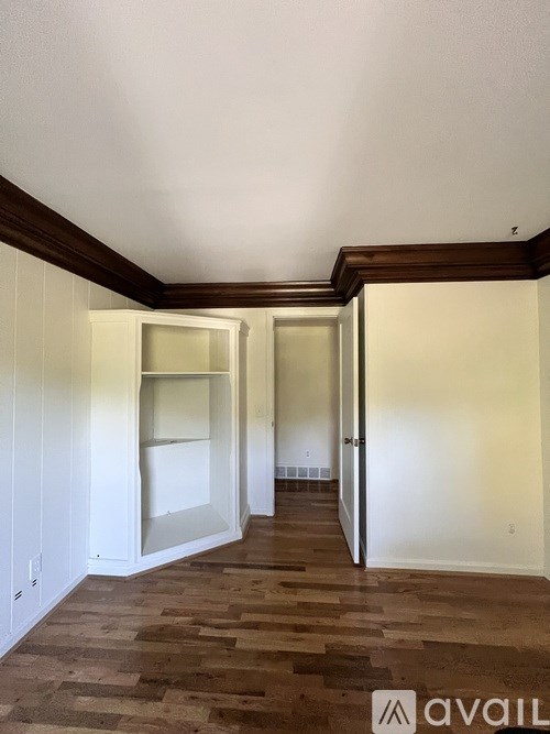 A room with wooden flooring and white walls, with a doorway leading to another room.