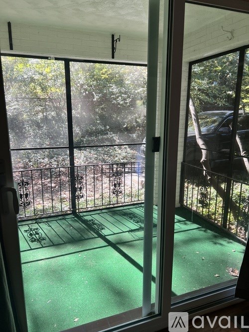 A balcony with a green floor and a view of trees and a fence.