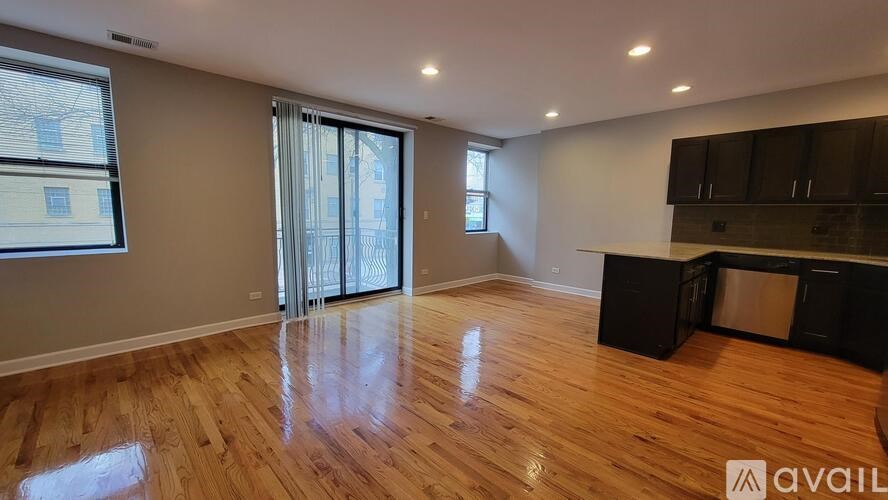 A spacious room with wooden flooring and a kitchen area with black cabinets.