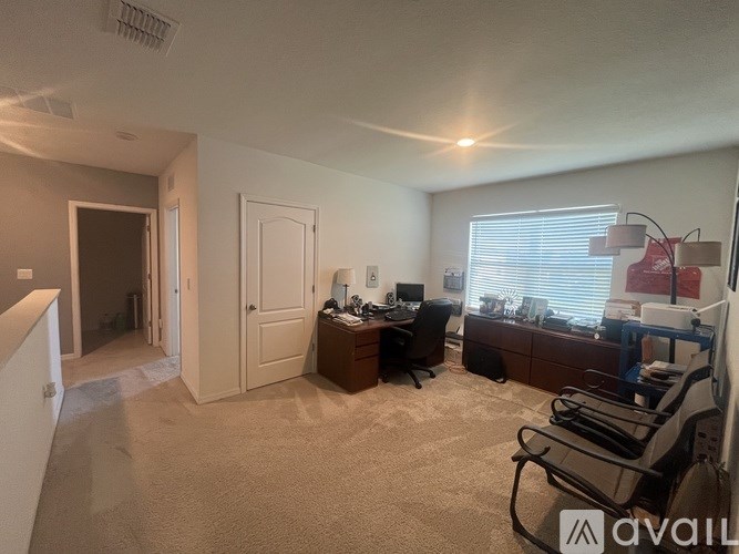 A room with a desk and chairs, a window with blinds, and a door leading to another room.