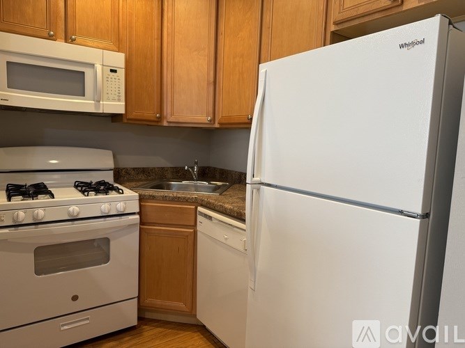 A white Whirlpool refrigerator stands in a kitchen with wooden cabinets and a white stove.