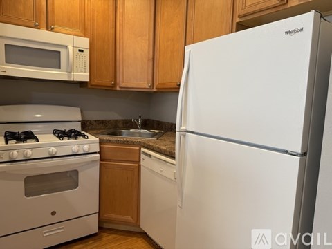 A white Whirlpool refrigerator stands in a kitchen with wooden cabinets and a white stove.