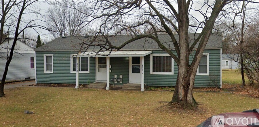 A green house with a white door and a tree in front.