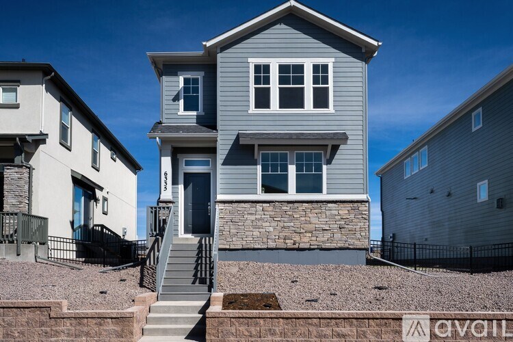 A grey house with a black fence and a stone wall in front.