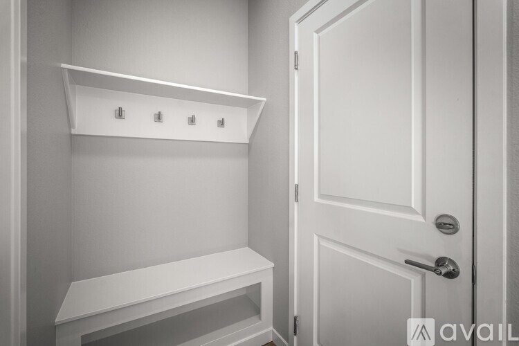 A white door is open to a small white room with a bench and shelves.