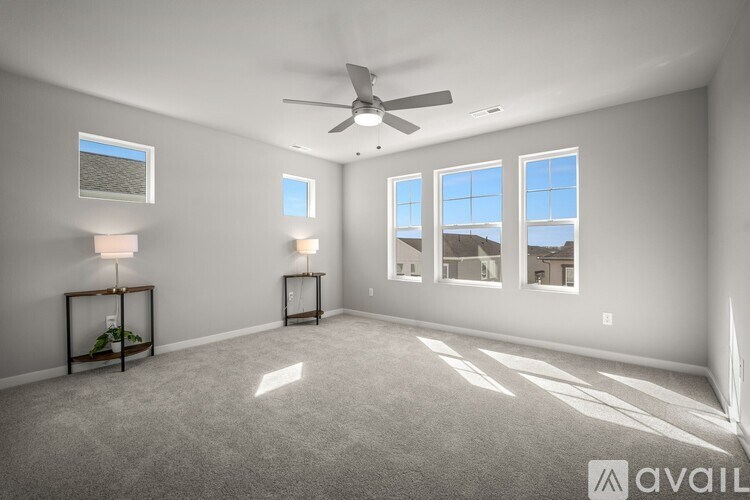 A spacious room with a ceiling fan, carpeted floor, and large windows.