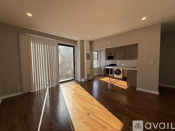 A spacious room with wooden flooring and a large window with blinds.