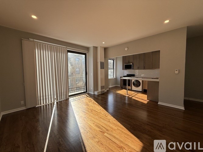 A spacious room with wooden flooring and a large window with blinds.