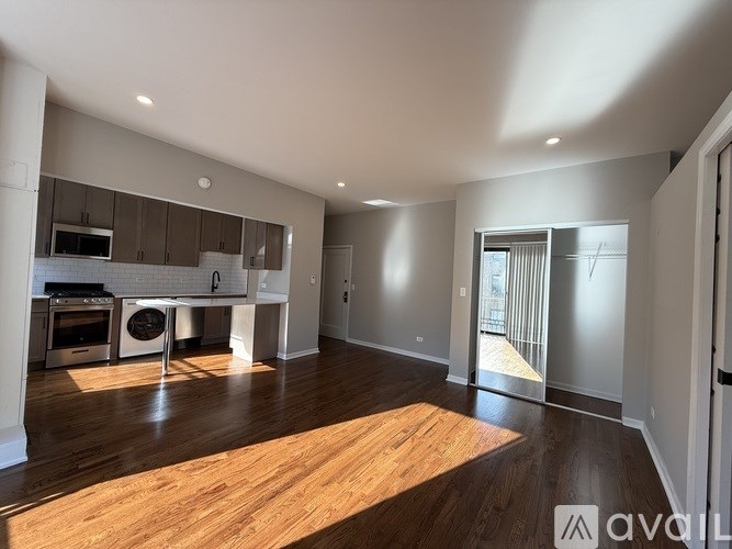 A spacious, empty room with wooden floors and a kitchen area in the background.
