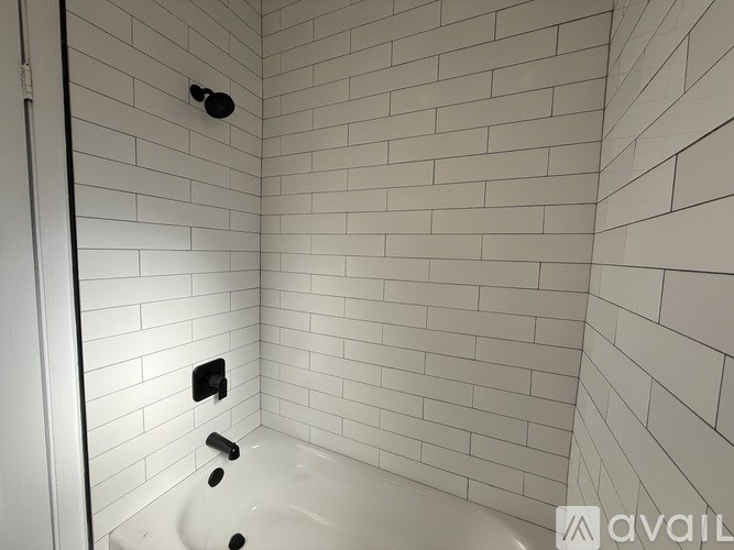 A white tiled bathroom with a tub and a shower head.